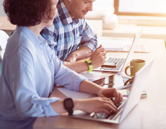 Work colleagues sitting at the table and using laptops while working in the office